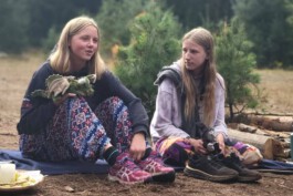 Zwei Jugendliche sitzen draußen im Wald und halten kleine Drachenfiguren aus Stoff in den Händen.