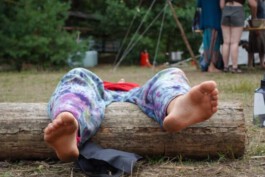 Eine Person liegt auf einer Decke im Wald und hat ihre nackten Füße auf einen liegenden Baumstamm gelegt.