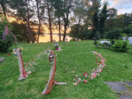 Mit Blüten und Bändern geschmückter Zeremonienplatz auf einer grünen Wiese am See im Abendlicht.