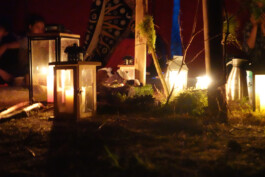 Brennendes Feuer und leuchtende Laternen auf einem mit Tüchern und Naturmaterialien gestalteten Ritualplatz bei Dunkelheit.