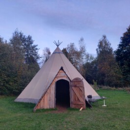 Großes Tipi auf einer Wiese zwischen Bäumen als gemeinschaftlicher Raum für das Trauerfeuer.