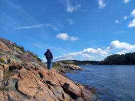 Eine barfüßige Person steht auf Felsen an einer Küste und blickt über das Wasser.