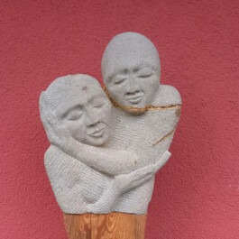 Steinskulptur zweier sich umarmender Figuren mit geschlossenen Augen und goldfarbenen Linien entlang der Bruchstellen.